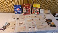 Display of three vintage stamp albums standing upright and multiple old envelopes and postcards laid out on a table.
