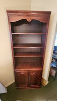 Full view of tall wooden bookcase with three shelves and bottom cabinet