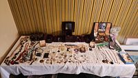 Full table of vintage jewelry and boxes spread out on white cloth showing vast variety of necklaces, rings, earrings, bracelets, and boxes.