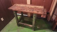 Full view of wooden work bench with green legs and worn wood top.