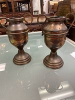 Two antique bronze vases, side by side, showing shape, handles, and finish with wear.