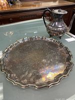 Side view of silver-plated tray and teapot on glass table showing tarnish and engraved detailing