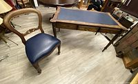 Overall view of antique wooden desk with navy leather inset top and matching chair with navy seat.