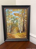 Full view of the framed painting of an autumn forest path showing birch trees and a leaf-covered trail.