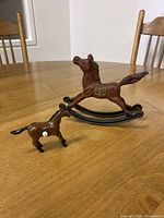 Two horse figurines on a wooden table: a larger cast iron rocking horse and a smaller plastic horse.