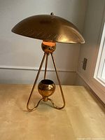 Brass table lamp with dome shade on tripod base, shot from front angle on light wood table