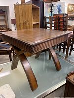 Photo of the whole square wood table showing top and curved crossed legs in a retail environment.
