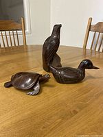 Three hand-carved wooden animal sculptures on table: eagle, turtle, duck