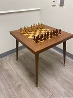 Full side view of the wooden chess table with chess pieces arranged on top, showing the tapered legs and overall design.