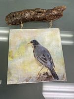 Front view of wooden wall art showing detailed painting of a dark bird on a rustic rope hanger attached to a natural wood branch.