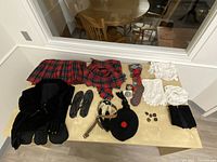 Full outfit items laid out on table including jacket, tartan kilt, sash, socks, shoes, belt, sporran, tam, brooches, medallions, and lace cuffs.