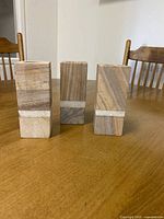 Front view of three stone candle holders standing upright on a wooden table, showing rectangular prism shape and natural beige stone with brown streaks.
