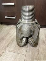 Front view of steel tricone drill bit showing three rotating cones with teeth and threaded connection top.