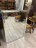 Full view of rectangular beveled wall mirror standing on floor reflecting furniture and artwork.