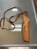 Top view of tan leather holster with adjustable strap laid out flat on glass surface showing strap and closure detail.