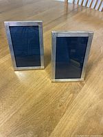 Two silver picture frames standing on wooden table, one in portrait and one slightly angled