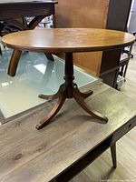 Side angle view of the oval wooden table showing the tabletop and pedestal base with brass foot caps.