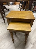 Two light wood nesting tables stacked with the smaller one under the larger one, showing the top and sides of both tables.