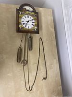 Full view of clock showing wooden frame, chains, weights, and pendulum.