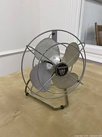 Front view of the vintage Torcan silver metal desk fan showing its four broad metal blades and circular wire guard.