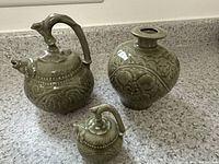 Three ceramic pieces on countertop with fish motif, two with spouts and handles, and one vase