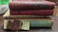 Stack of five vintage hardcover books showing spine titles: 'Tom Brown's School Days', 'Economic and Philosophic Manuscripts', and others with worn, taped, and faded covers.