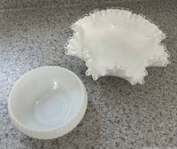 Two antique milk glass bowls on countertop, larger with ruffled clear edge and smaller ribbed bowl