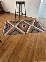 Full view of antique metal stool placed on Navajo-style rug showing overall size relationship