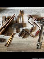 Various antique wooden clamps, hand drills, square tool and part of collapsible yardstick laid on floor