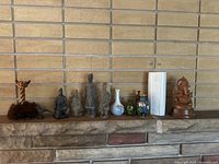 Front view of all Asian decor pieces arranged on a stone shelf, showing clay/cement human figures, various vases, bird figurine, wooden elephant, and twisted wood sculpture.