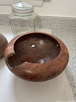 Wooden bowl showing natural finish with cracks and chips, positioned in front of glass cookie jar