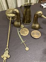 Overview of brass decor items including duck bookends, jug, bell, letter opener, caster and desk calendar on a dark surface.