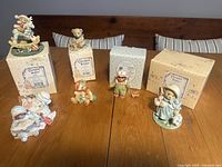 Seven Cherished Teddies figurines displayed with their original boxes on a wooden table.