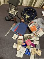 Small vintage mantel clock with hourglass, three smoking pipes, large assorted vintage matchbooks, grammar school cap with yellow piping and emblem, British Army Hampshire Yeomanry Carabiniers cap badge.