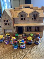 Photo showing the wooden dollhouse with 13 Little People characters arranged in front, highlighting the condition of the house and variety of figurines.