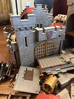 Front view of large gray castle wall with golden barred gate and blocky battlements, scattered parts in foreground