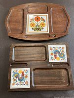 Two vintage wooden charcuterie boards displayed flat, showing carved compartments and colorful decorative ceramic tiles with floral and rooster motifs.