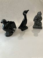 Three soapstone carvings standing side by side including two birds and one human figure.