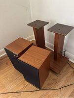Two wooden Castle bookshelf speakers and two wooden stands positioned near a wall on hardwood floor.