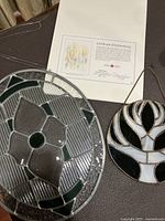 Photo of large oval stained glass piece with floral center along with circular tree stained glass piece and Certificate of Authenticity for the artwork.