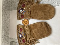 Full view of suede mittens laid flat showing brown color, fringe edges, and beadwork