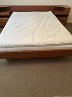 Front view of assembled teak queen bed frame with headboard, mattress and attached side tables