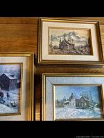 Overview of three framed snowy landscape paintings on wooden floor