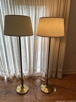 Two vintage brass floor lamps side by side. One lamp is illuminated.