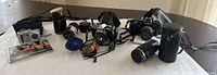 Overview of multiple vintage cameras, lenses and accessories including Minolta SR-T 101 with lens, Olympus SLR, compact digital camera, telephoto lens with case, filters, manual and headphones