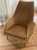 Front angled view of mustard upholstered vintage chair showing button tufting, cushioned seat, and wooden legs.