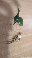 Top view of green jade flying goose pin and 12K gold carved rose pin on wood surface