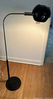 Full length of vintage floor lamp showing black round base, vertical stand and horizontal adjustable arm with spherical black metal shade.