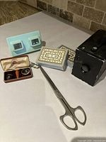Photo of all items in lot showing Kodak Brownie #2 camera, scissors, playing cards, blue Simplex stereoscope viewer, and contact lenses in case