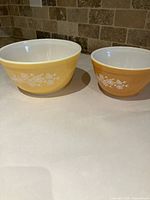 Two vintage Pyrex mixing bowls in yellow and mustard with white floral patterns.